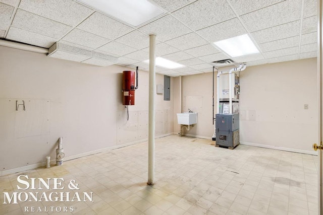 basement with electric panel, a drop ceiling, heating unit, and sink