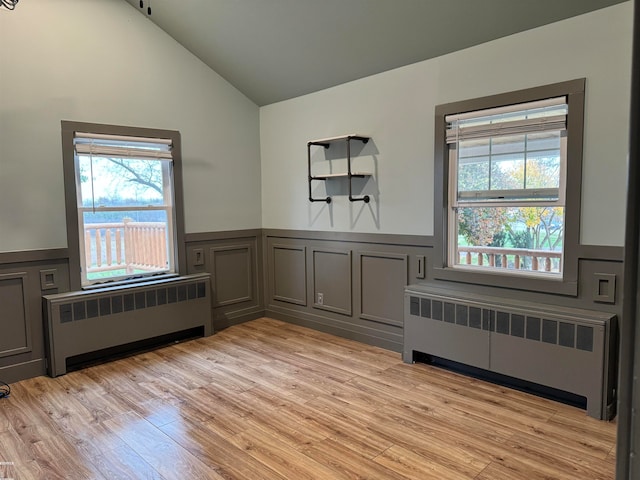 empty room featuring radiator, light hardwood / wood-style floors, and vaulted ceiling