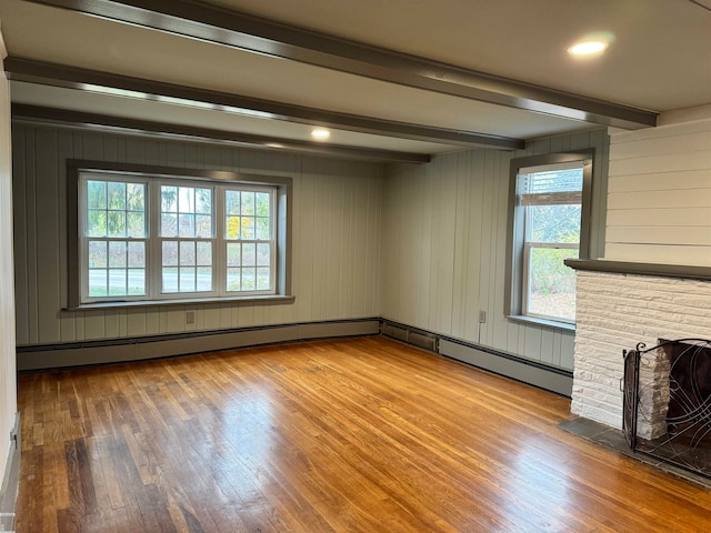 unfurnished living room featuring a wealth of natural light, beamed ceiling, wood-type flooring, and a brick fireplace