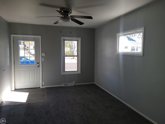 foyer featuring a wealth of natural light, ceiling fan, and dark colored carpet