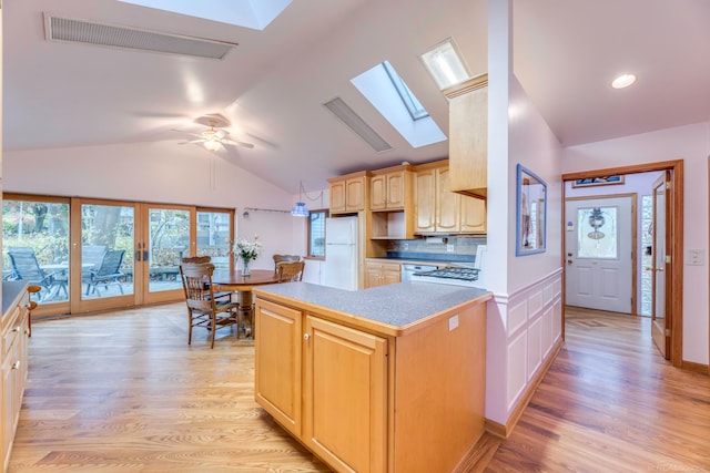 kitchen featuring decorative backsplash, light brown cabinets, light wood-type flooring, and vaulted ceiling with skylight