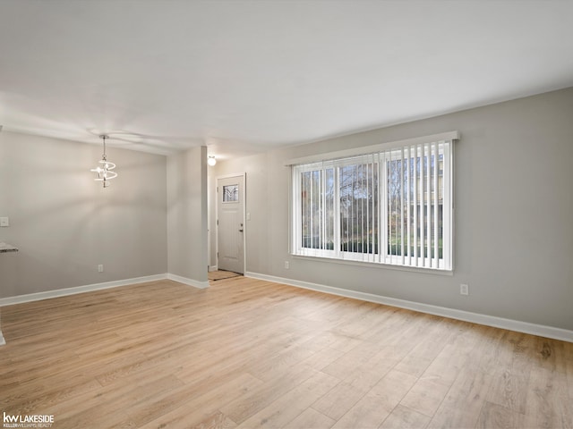 unfurnished room featuring an inviting chandelier and light wood-type flooring