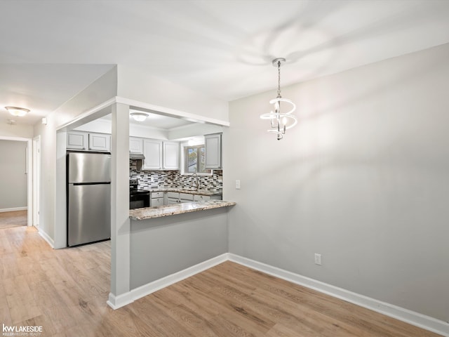 kitchen featuring black electric range oven, hanging light fixtures, tasteful backsplash, light hardwood / wood-style floors, and stainless steel refrigerator