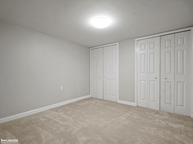 unfurnished bedroom with multiple closets and light colored carpet