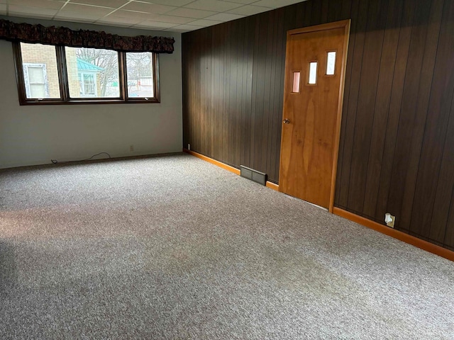 carpeted empty room featuring a paneled ceiling and wood walls