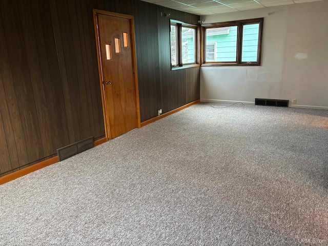 carpeted empty room featuring wood walls