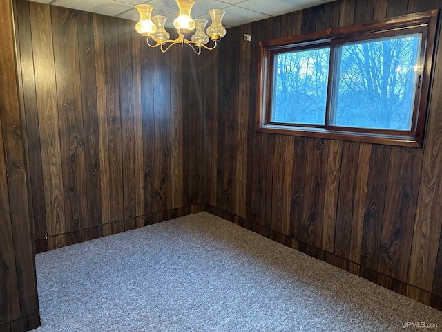 carpeted empty room featuring wooden walls and an inviting chandelier