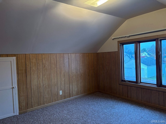 additional living space with carpet floors, vaulted ceiling, and wood walls