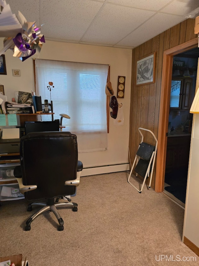 carpeted office with a drop ceiling, a baseboard heating unit, and wood walls