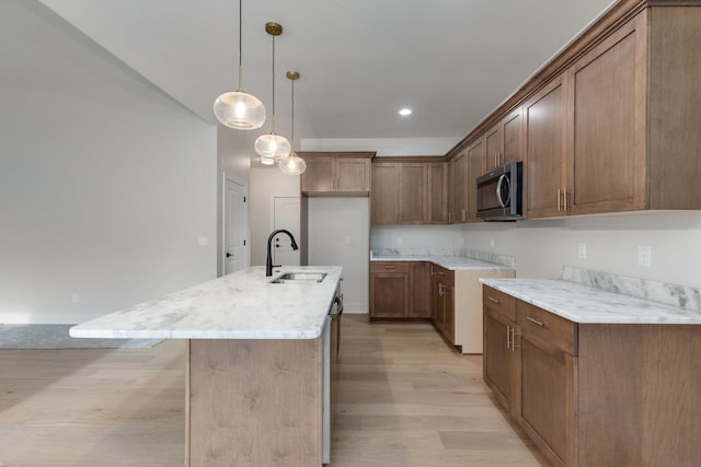 kitchen featuring light wood-type flooring, stainless steel appliances, sink, a center island with sink, and hanging light fixtures