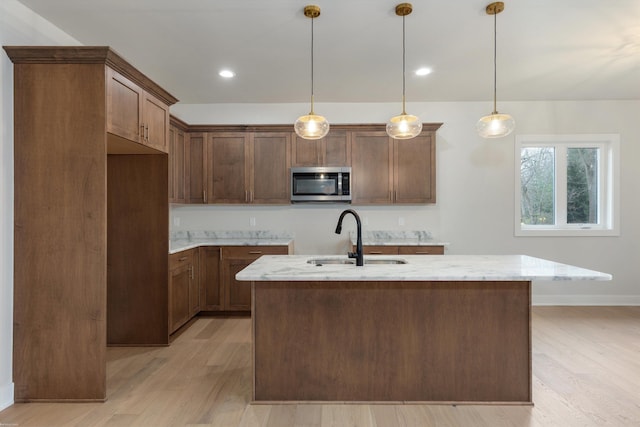 kitchen featuring pendant lighting, a kitchen island with sink, sink, light stone countertops, and light hardwood / wood-style floors