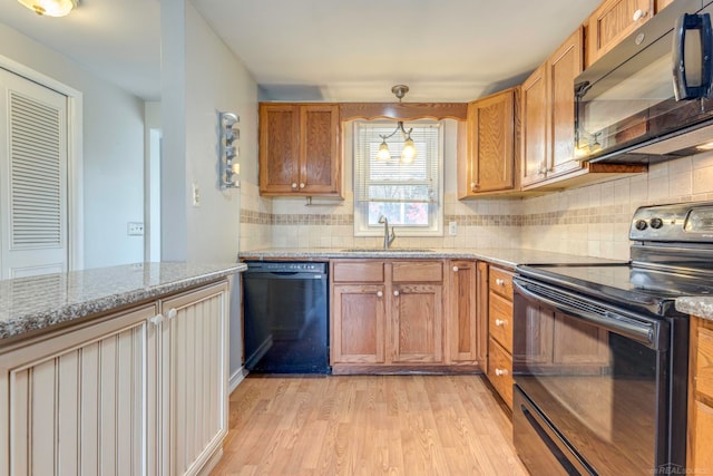 kitchen featuring light stone counters, sink, black appliances, and light hardwood / wood-style flooring