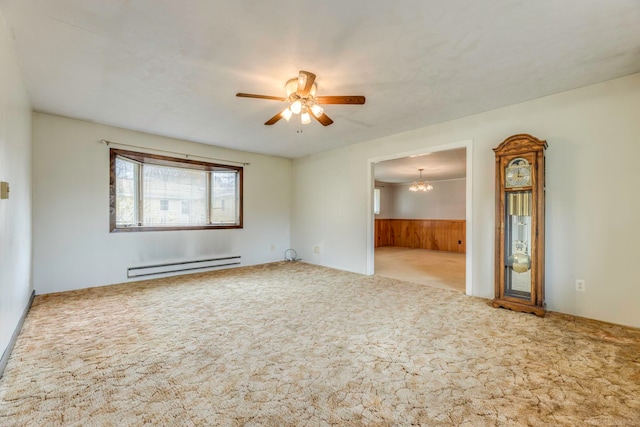 carpeted spare room featuring ceiling fan with notable chandelier, baseboard heating, and wooden walls