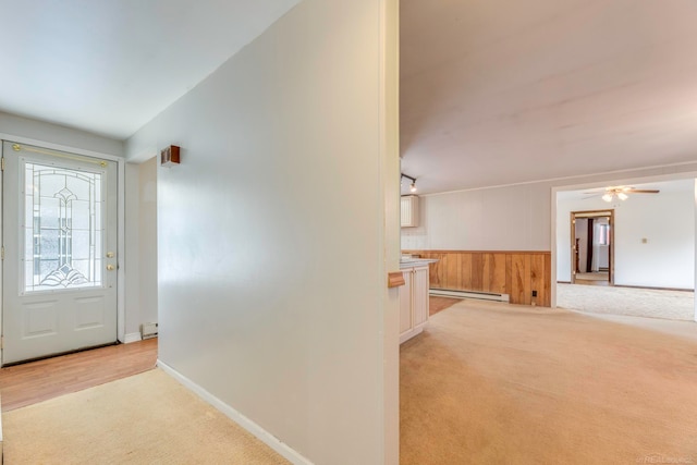 carpeted foyer featuring baseboard heating, wooden walls, and ceiling fan