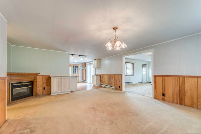 unfurnished living room with rail lighting, a baseboard radiator, an inviting chandelier, light carpet, and ornamental molding