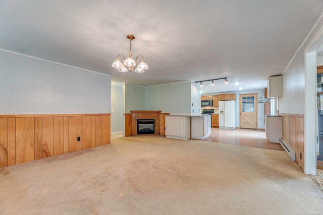 unfurnished living room featuring light carpet, an inviting chandelier, rail lighting, wooden walls, and baseboard heating