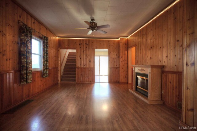 unfurnished living room featuring dark hardwood / wood-style floors, ceiling fan, and wood walls