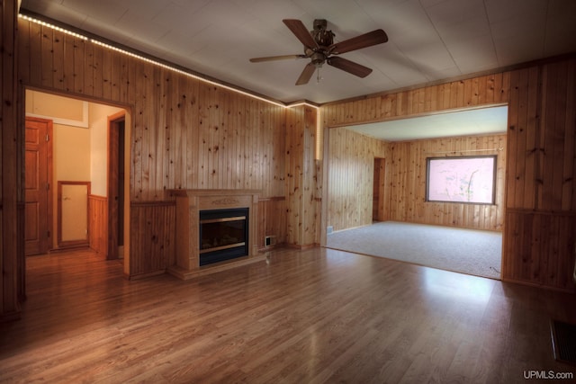 unfurnished living room featuring wood-type flooring, ceiling fan, and wood walls