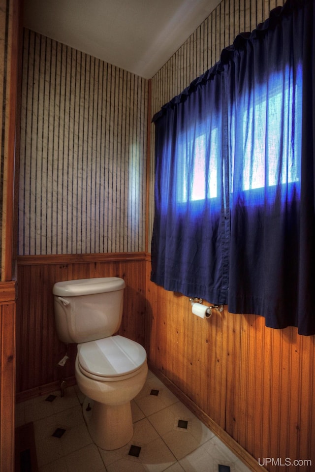 bathroom featuring tile patterned floors, wood walls, and toilet