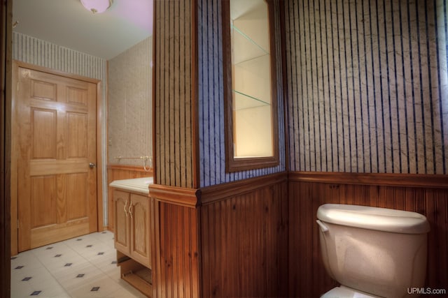 bathroom featuring vanity, toilet, and wood walls