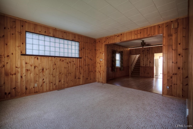 empty room with carpet flooring, ceiling fan, and wood walls