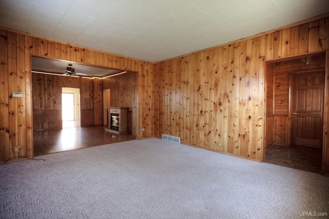 unfurnished room featuring wooden walls, ceiling fan, and dark carpet