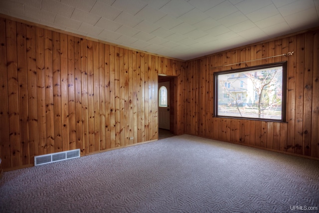 carpeted empty room featuring wooden walls