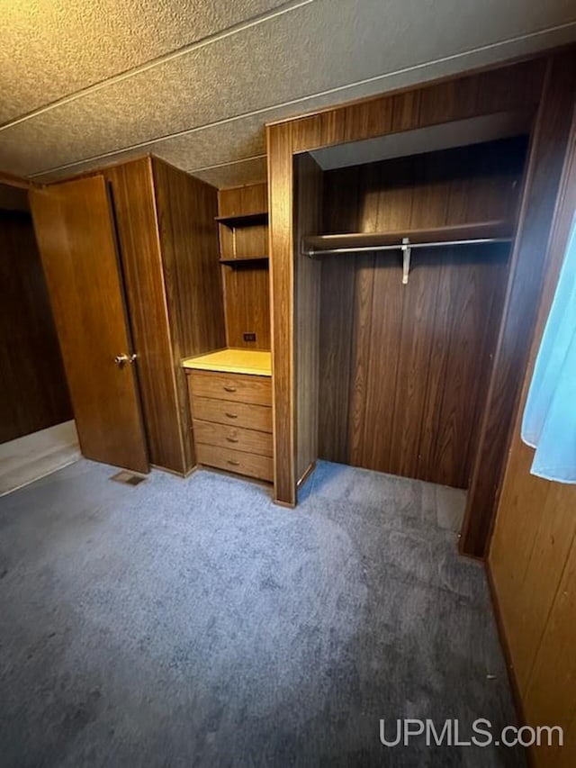 unfurnished bedroom with carpet flooring, wooden walls, a closet, and a textured ceiling