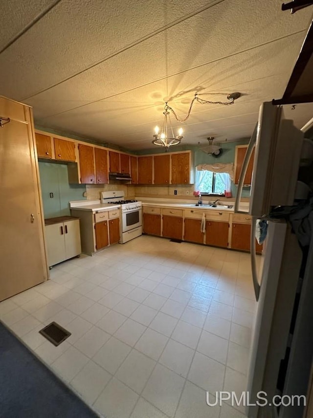 kitchen featuring a notable chandelier, sink, white appliances, and hanging light fixtures