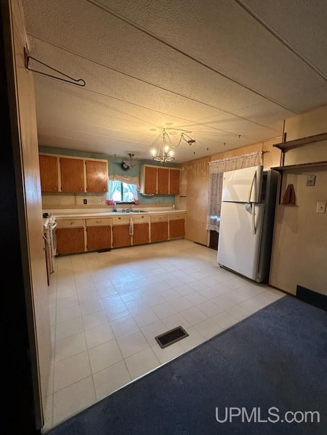 kitchen featuring light tile patterned floors, white range, stainless steel refrigerator, and a notable chandelier