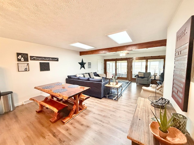 living room featuring a skylight, light hardwood / wood-style floors, and a textured ceiling