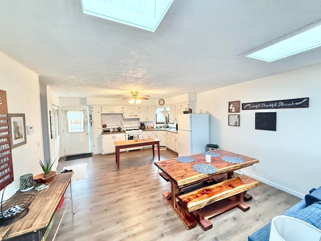 dining area with a skylight, ceiling fan, a textured ceiling, and light wood-type flooring