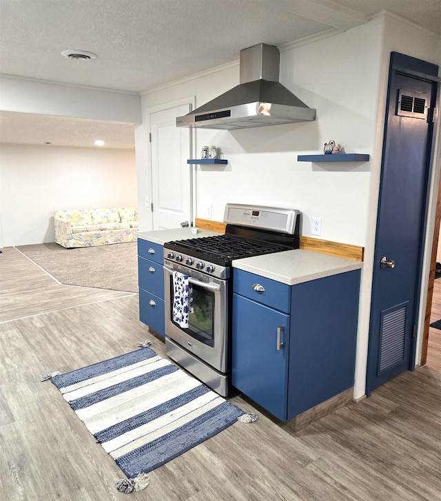 kitchen featuring wall chimney range hood, blue cabinets, hardwood / wood-style floors, a textured ceiling, and stainless steel range with gas stovetop