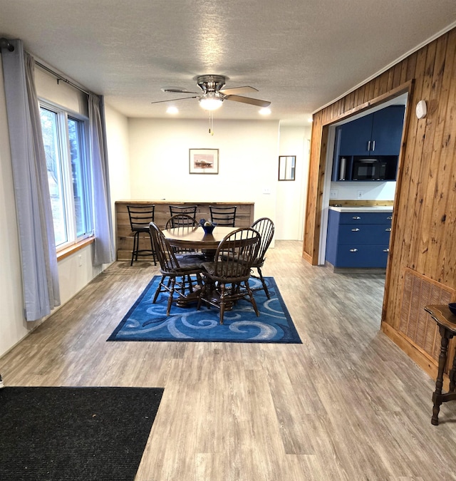 dining area featuring wood walls, ceiling fan, wood-type flooring, and a textured ceiling