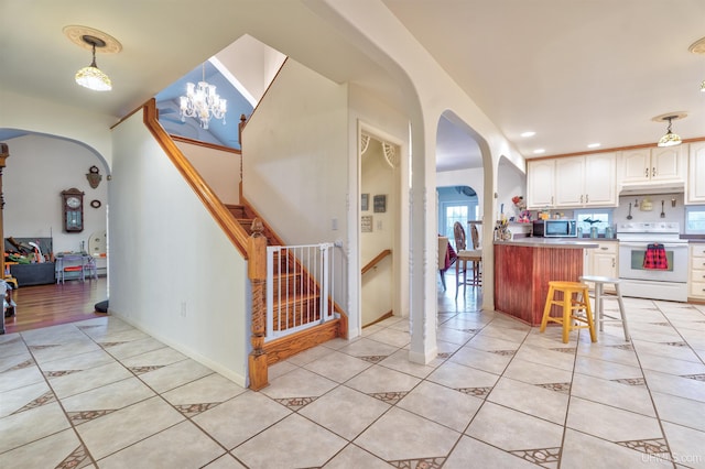 kitchen featuring pendant lighting, an inviting chandelier, a kitchen breakfast bar, white electric stove, and light tile patterned floors