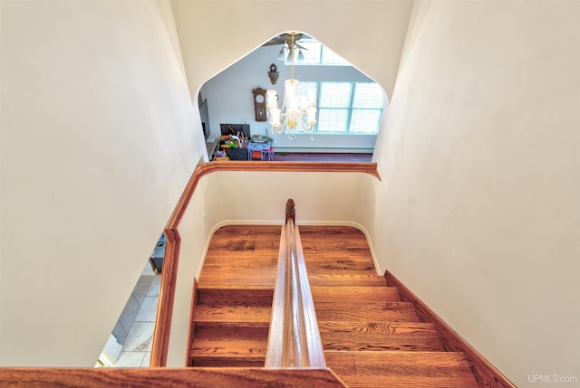 staircase with ceiling fan with notable chandelier and hardwood / wood-style flooring