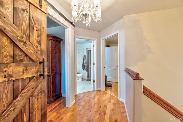 corridor featuring a barn door, light hardwood / wood-style flooring, and an inviting chandelier