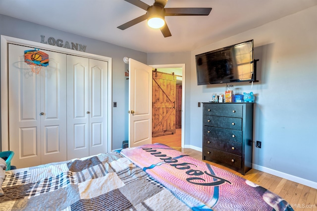 bedroom featuring ceiling fan, a barn door, light hardwood / wood-style flooring, and a closet