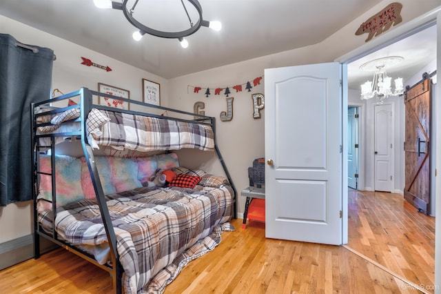 bedroom with a chandelier, a barn door, and light hardwood / wood-style floors