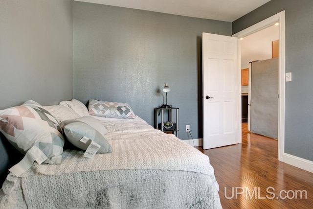 bedroom with stainless steel fridge and dark wood-type flooring