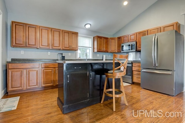 kitchen featuring stainless steel appliances, a kitchen breakfast bar, light hardwood / wood-style floors, lofted ceiling, and a kitchen island