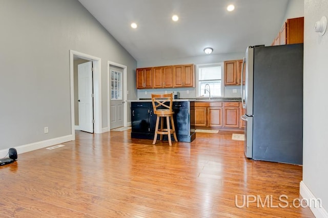 kitchen featuring stainless steel refrigerator, a center island, light hardwood / wood-style flooring, high vaulted ceiling, and a breakfast bar area