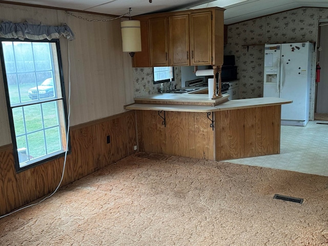 kitchen with pendant lighting, lofted ceiling, white fridge with ice dispenser, plenty of natural light, and kitchen peninsula