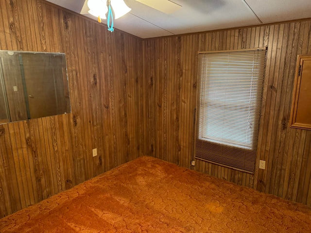 empty room with carpet flooring, ceiling fan, and wooden walls