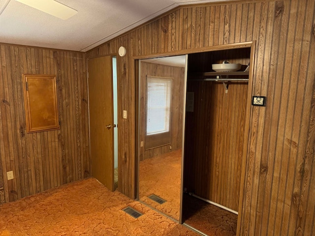 corridor featuring dark carpet, a textured ceiling, vaulted ceiling, and wood walls