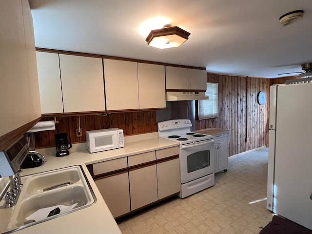 kitchen with white appliances, wooden walls, and sink