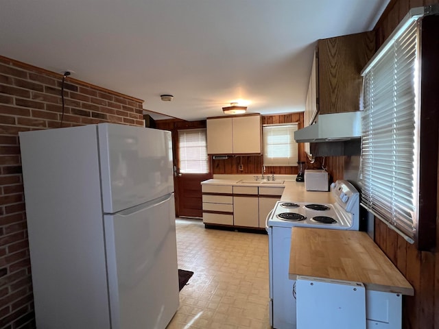 kitchen with sink, white appliances, brick wall, and range hood