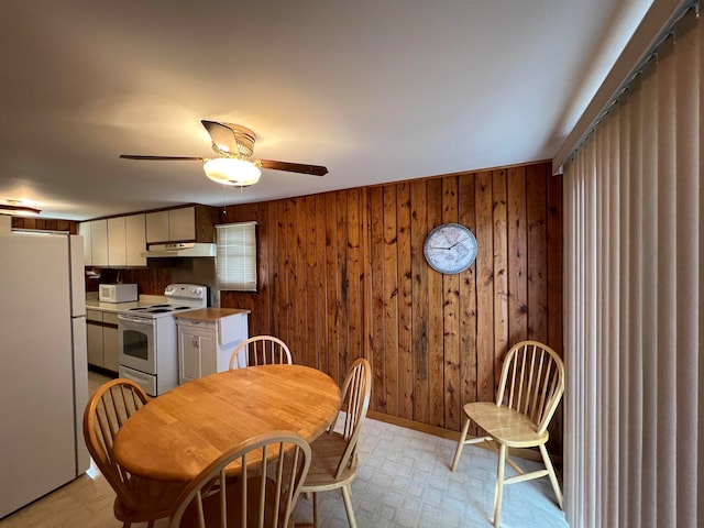 dining area with ceiling fan and wood walls