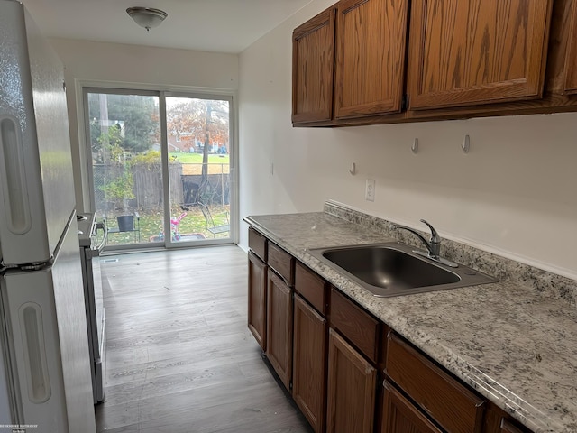 kitchen featuring white fridge, light stone counters, light hardwood / wood-style floors, and sink