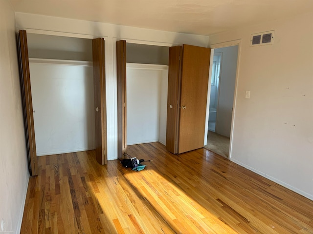 unfurnished bedroom with wood-type flooring and multiple closets